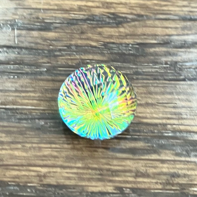 May include: A round iridescent glass bead with a swirling pattern of green, blue, and yellow.