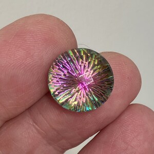 May include: A round, iridescent gemstone with a starburst pattern in shades of pink, green, and blue. The gemstone is approximately 1 inch in diameter.