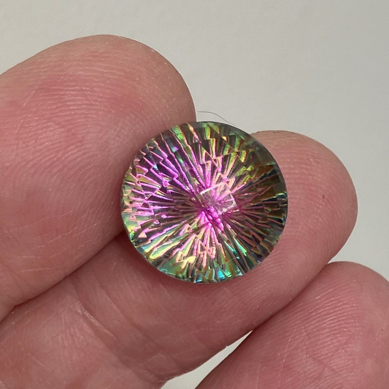 May include: A round, iridescent gemstone with a starburst pattern in shades of pink, green, and blue. The gemstone is approximately 1 inch in diameter.