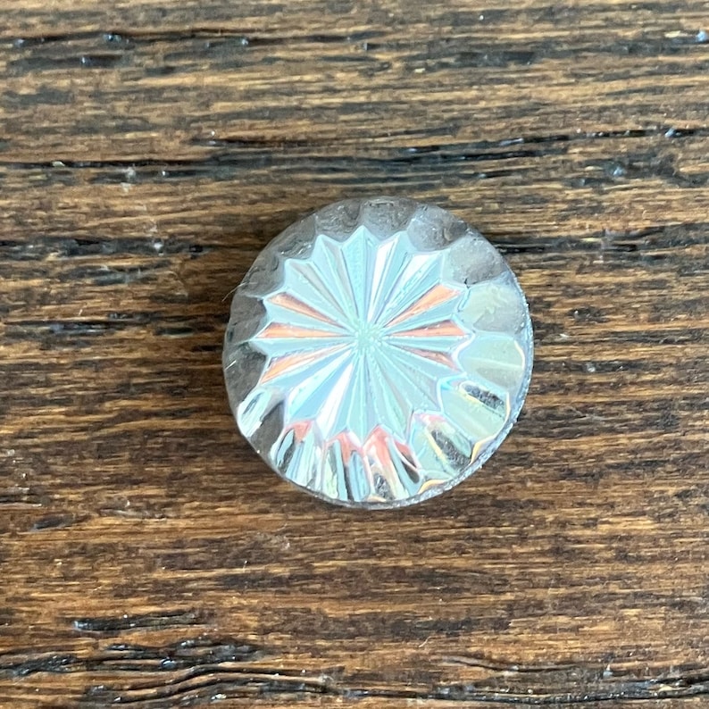 May include: A silver-toned, round, decorative knob with a starburst pattern.