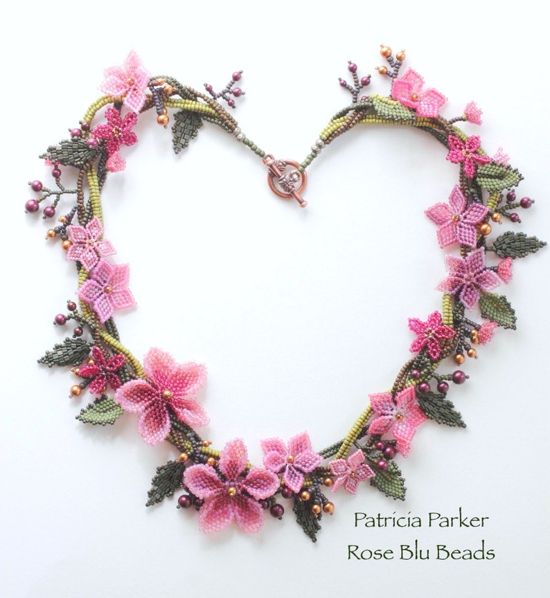May include: A delicate beaded necklace featuring pink and green flowers, with a copper clasp. The necklace is made by Patricia Parker, Rose Blu Beads.