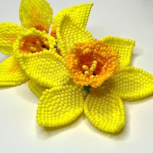 May include: A cluster of yellow and orange beaded daffodils. The flowers are made of small beads and have a realistic appearance.