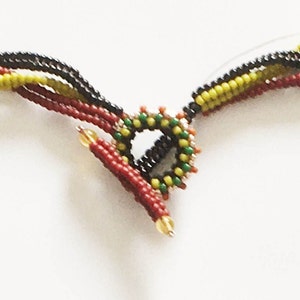 May include: A multi-strand beaded necklace with a colourful, circular clasp. The necklace is made of black, red, yellow, and green beads.