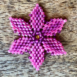 May include: A pink and purple beaded flower with a six-pointed star shape.