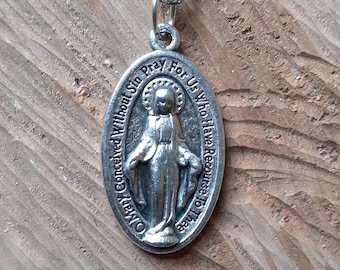 Op de afbeelding: Een zilveren ketting met een zilveren ovale hanger met een afbeelding van de Maagd Maria. De hanger heeft de inscriptie "O Maria, onbevlekt ontvangen, bid voor ons die onze toevlucht tot u nemen".