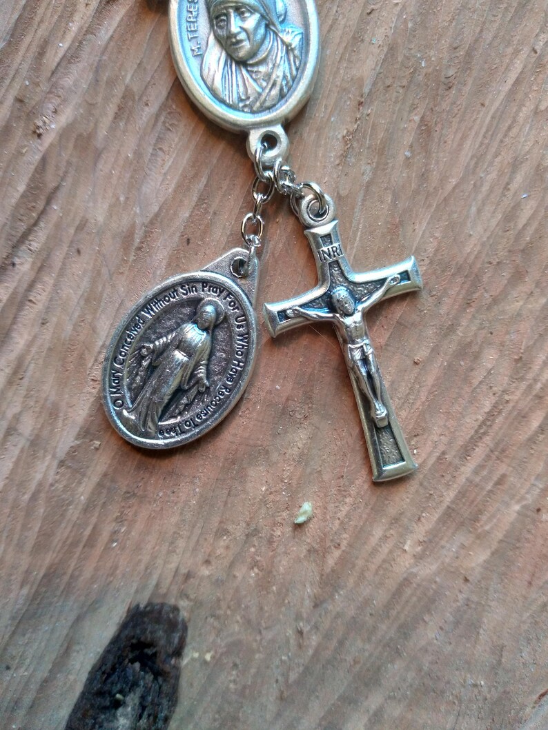 Op de afbeelding: Zilveren rozenkrans met een zilveren kruisbeeld, een zilveren medaille van de Maagd Maria en een zilveren medaille van Moeder Teresa. De medailles hebben inscripties in het Engels.