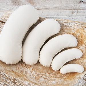 May include: Set of six crescent-shaped pillows in various sizes, made of white fabric, arranged in a graduated pattern on a wooden surface.