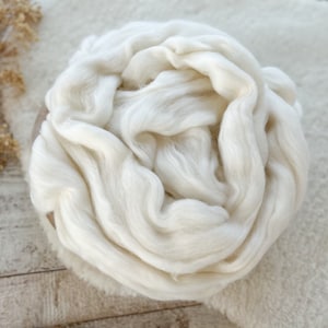 Puede incluir: Un telón de fondo de tela blanca, esponjosa y suave para fotografía de recién nacidos. La tela está dispuesta en forma circular, creando un ambiente acogedor y agradable para una sesión de fotos de bebé.