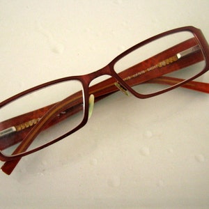以下が含まれることがあります： 薄い金の金属フレームが付いた、茶色の長方形の眼鏡です。