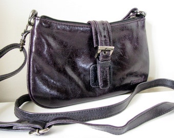 May include: A small, dark purple leather crossbody bag with a silver buckle and a silver chain detail. The bag has a zipper closure and a brand name "Frame" on the front.