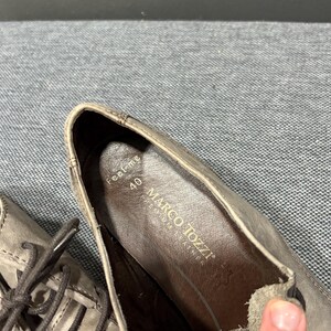 May include: Close-up of a pair of gray leather shoes. The shoe's interior displays the brand name "MARCO TOZZI" and size 40. The shoes have laces and a textured appearance.