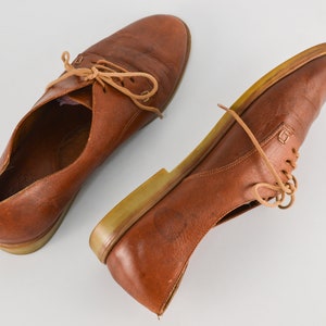 May include: A pair of brown leather lace-up shoes with a light brown sole.