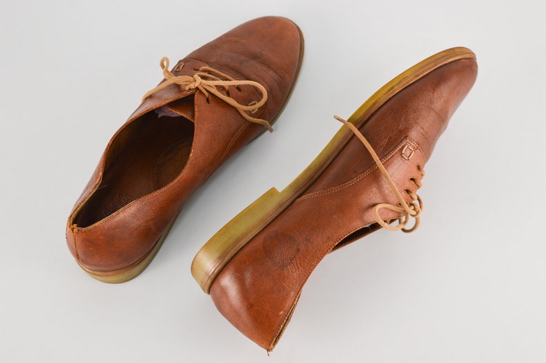 May include: A pair of brown leather lace-up shoes with a light brown sole.