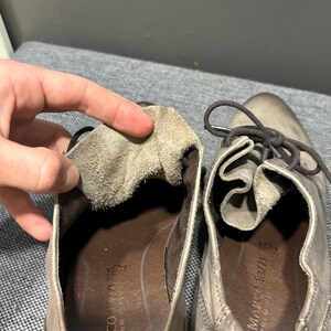 May include: Close-up of a pair of gray leather shoes with laces. The interior of one shoe is exposed, revealing a soft, textured lining. The brand name "MARCO TOZZI PREMIUM" is visible on the insole.