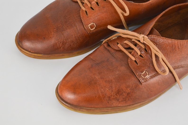May include: A pair of brown leather lace-up shoes with a rounded toe and a low heel.
