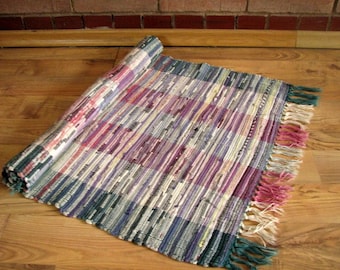 May include: A colorful woven rug with a striped pattern in shades of purple, pink, blue, and green. The rug has a fringe border.