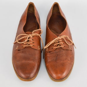 May include: A pair of brown leather lace-up shoes with tan laces. The shoes have a rounded toe and a low heel.