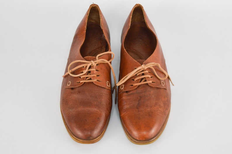 May include: A pair of brown leather lace-up shoes with tan laces. The shoes have a rounded toe and a low heel.