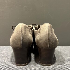 May include: A pair of brown leather heeled shoes with laces. The shoes have a rounded toe and a dark brown block heel. The leather has a distressed appearance. The shoes are viewed from the back.