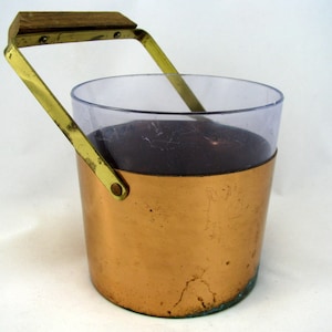 May include: A copper ice bucket with a clear glass liner and a brass handle with a wooden top.