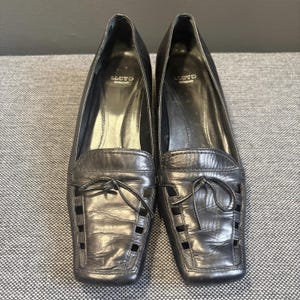 May include: A pair of black leather loafers with square toes. The shoes have a decorative cut-out design on the vamp and a small bow detail. The brand name "LLOYD GERMANY" is visible inside the shoe.