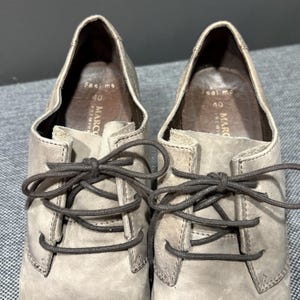May include: A pair of light gray leather oxford shoes with brown laces. The shoes have a low heel and the interior is stamped with "Feel me" and "40". The brand name "MARCO PREMIUM" is also visible.