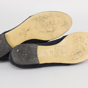 Peut inclure: Une paire de ballerines en daim bleu marine avec une semelle cr&egrave;me. Les semelles sont marqu&eacute;es de la taille "38" et du nom de la marque.