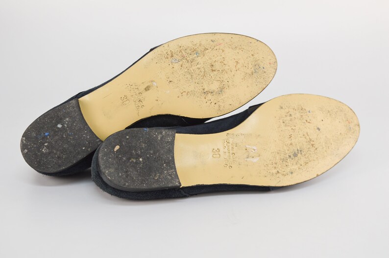 Peut inclure: Une paire de ballerines en daim bleu marine avec une semelle cr&egrave;me. Les semelles sont marqu&eacute;es de la taille "38" et du nom de la marque.