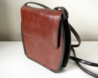 May include: A brown leather crossbody bag with a black strap and the text "Ally & Son" embossed on the front.