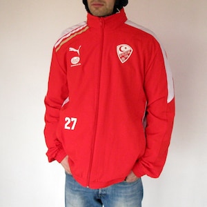 Peut inclure: Veste de survêtement rouge et blanche avec un logo Puma et le texte "TURKIYE 1923" sur le devant. Le numéro "27" est imprimé sur le côté gauche de la veste.