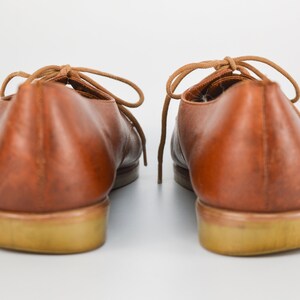 May include: A pair of brown leather lace-up shoes with a light brown sole.