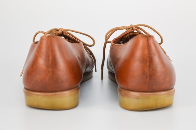 May include: A pair of brown leather lace-up shoes with a light brown sole.