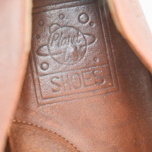May include: Close-up of the inside of a brown leather shoe with the words "Planet Shoes" and a graphic of a planet inside a circle.