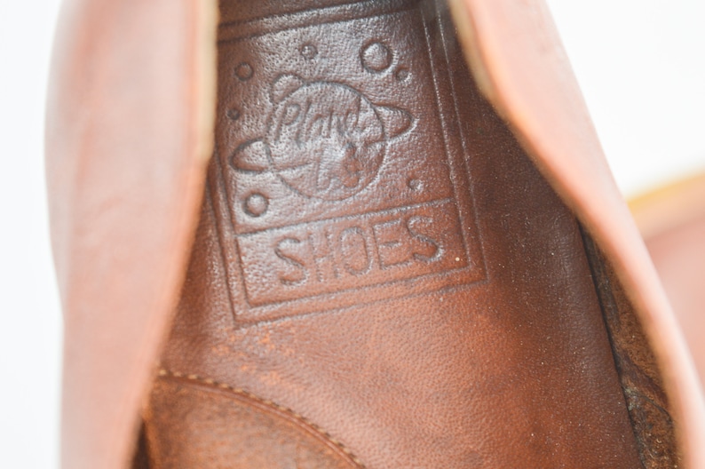 May include: Close-up of the inside of a brown leather shoe with the words "Planet Shoes" and a graphic of a planet inside a circle.