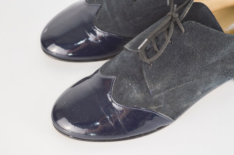 Peut inclure: Une paire de chaussures en cuir bleu marine avec une fermeture &agrave; lacets. Les chaussures ont un bout en cuir verni et une tige en daim.