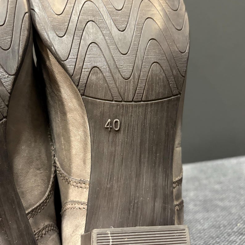 May include: Close-up of the sole of a gray shoe. The sole has a textured, wave-like pattern. The number "40" is stamped on the heel of the shoe. The shoe appears to be made of leather.