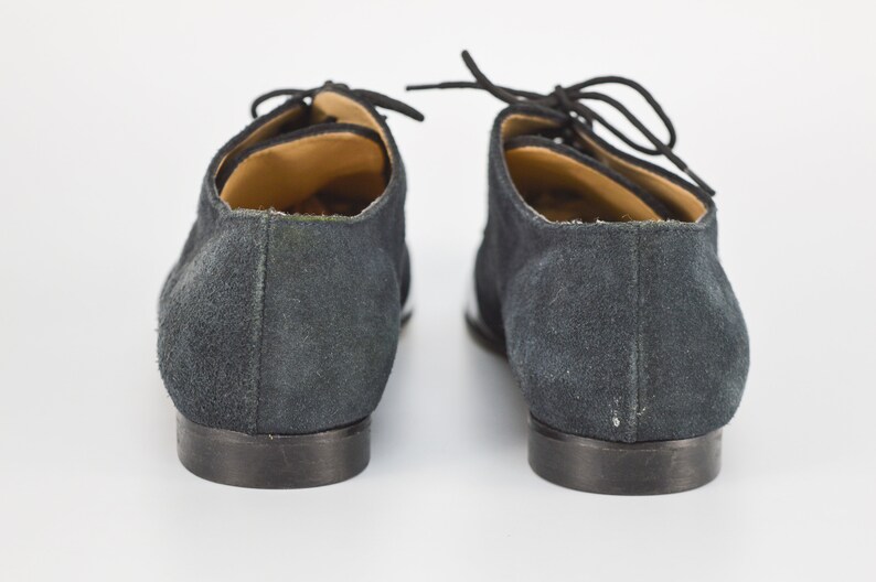 Peut inclure: Une paire de chaussures en daim noir &agrave; lacets avec des bordures blanches sur les c&ocirc;t&eacute;s. Les chaussures ont une pointe arrondie et un talon bas.
