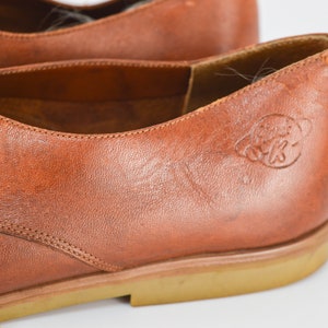 May include: Close-up of a brown leather oxford shoe with a brown rubber sole. The shoe has a lace-up closure and a small logo on the side that says "Globe Trotters".