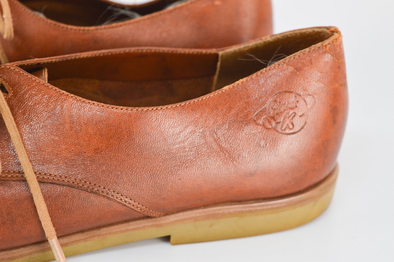 May include: Close-up of a brown leather oxford shoe with a brown rubber sole. The shoe has a lace-up closure and a small logo on the side that says "Globe Trotters".