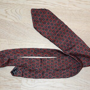 Puede incluir: Una corbata de seda roja y azul con un diseño geométrico. La corbata está doblada y anudada.