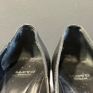 May include: Close-up of two black leather shoes. The interior of each shoe is visible, with the brand name "LLOYD GERMANY" stamped in white. The shoes appear worn, with visible creases and wear.