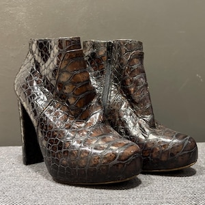 May include: A pair of brown, textured ankle boots with a platform sole and block heels. The boots have a reptile-like pattern and a zipper closure. The heels are approximately 4 inches high.
