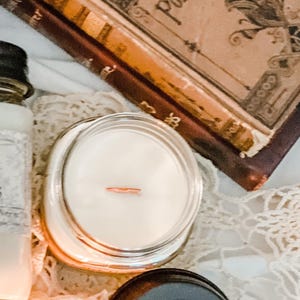 Old Books scented, Wooden Wick Soy Candle in a mason jar. The mysterious and cozy scent of old vintage books, libraries and dusty shelves full of leather bound wonders.  Crafted by Teresa Lynns Simple Luxuries in Monrovia, Indiana.  Pictured with a stack of antique books from her collection.