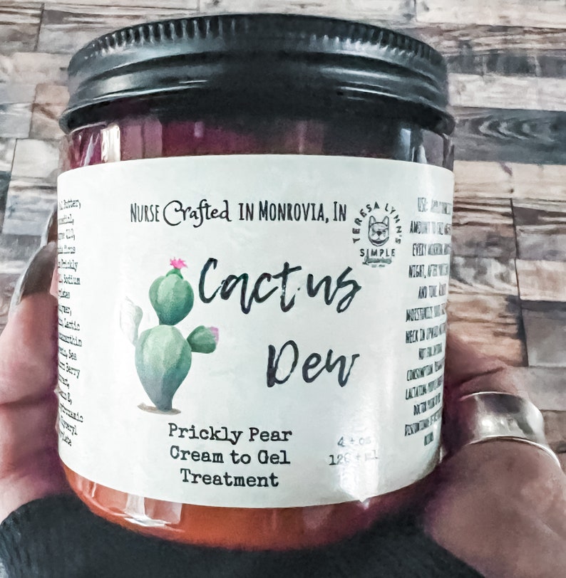 A glass jar with a black lid and a white label. The label says 'NURSE Crafted IN MONROVIA, IN TERESA LYNN'S SIMPLE Cactus Dew Prickly Pear Cream to Gel Treatment and has a green cactus illustration.