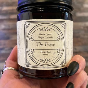 The Fence, Protection and Boundary Setting Wooden Wick Soy Wax Candle in a dark Amber jar with a metal lid, held in Teresas Hand.Cedar and Redwood cleansing and protection blessings.
Cedar wood and Redwood essential oil, when used for charms are often referred to as “The fence” due to its powerful characteristic of forcing harmful projections out and keeping protective powers in. Crafted in Monrovia, Indiana at Teresa Lynns Simple Luxuries