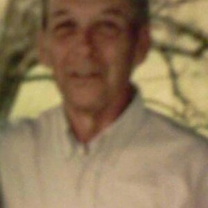 May include: A man wearing a light beige button-down shirt. He is smiling and looking at the camera.