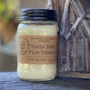 May include: A clear glass jar candle with a black lid and a brown label that reads "Uncle Ted's Pipe Tobacco" and "100% Soy Wax".