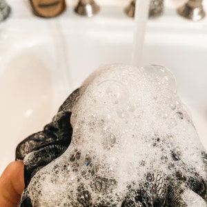 A black shower poof covered in bubbles, demonstrates the use of this product.