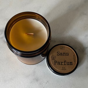 May include: A brown glass jar candle with a wooden wick and white wax. The lid is off, revealing the candle. The lid has the words "Sans Parfum" printed on it, along with other text. The candle is 8 oz / 240 gr.