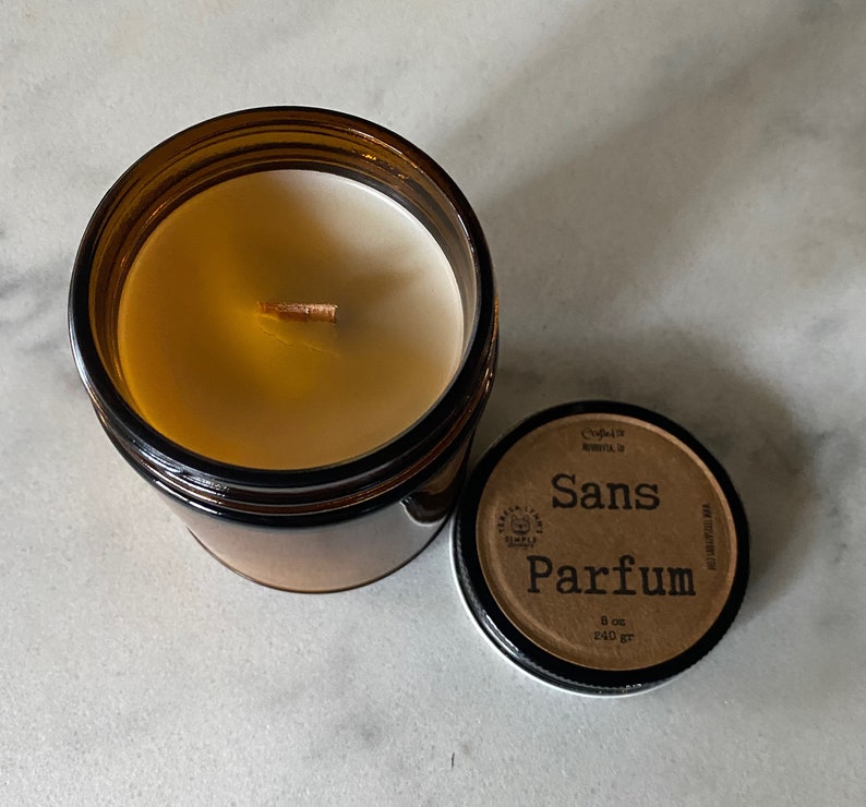May include: A brown glass jar candle with a wooden wick and white wax. The lid is off, revealing the candle. The lid has the words "Sans Parfum" printed on it, along with other text. The candle is 8 oz / 240 gr.